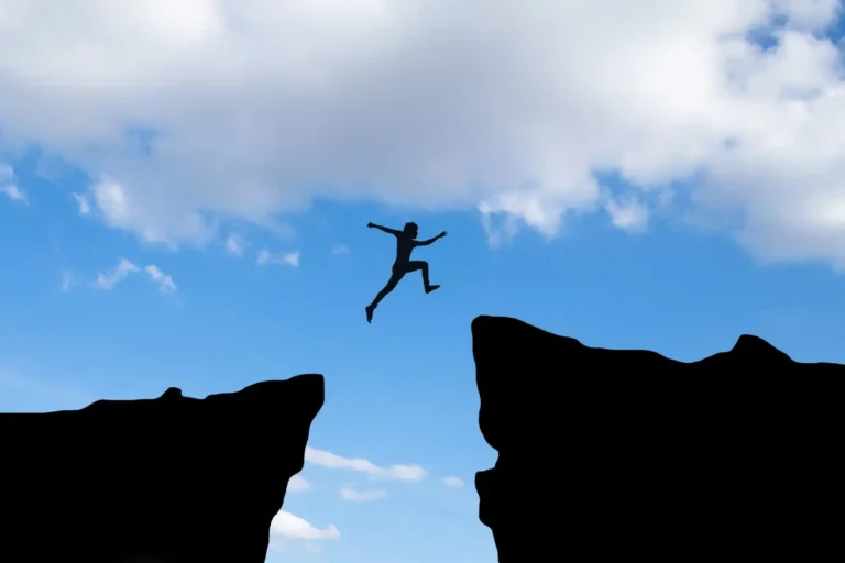 an image of a male hiker leaping across a big gash or gap in the mountain, symbolising What Non-Compliance Actually Costs with AML/CTF Penalties