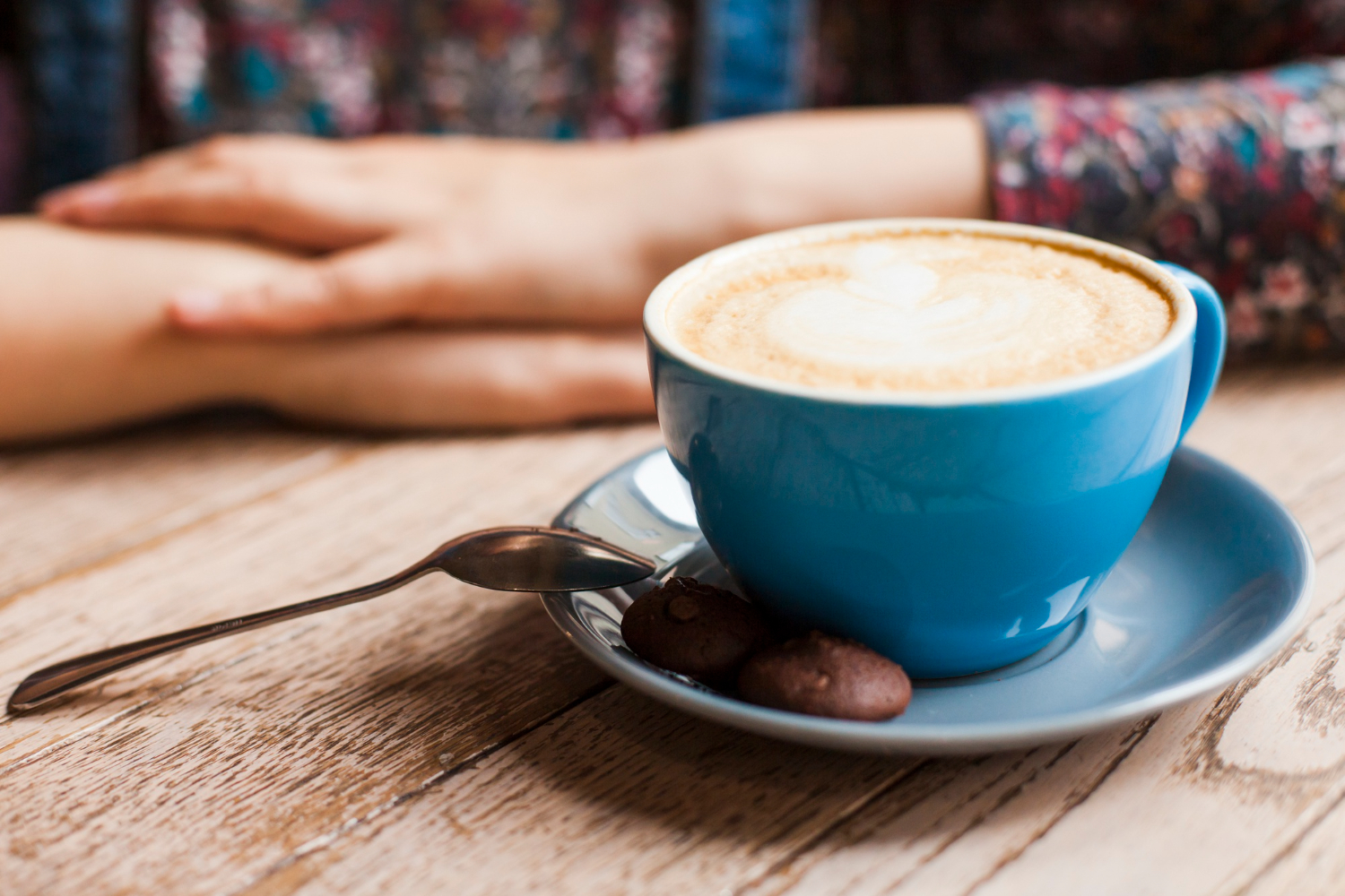 an image of a blue cup filled with cappuccino on a blue saucer with a small piece of chocolate and woman at the background, symbolising the stress-free process of Small Business CGT Concessions with DBA Advisory